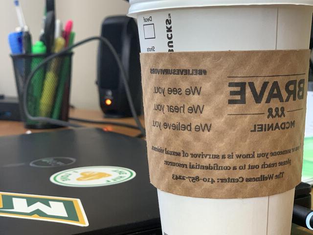星巴克咖啡杯和BRAVE-McDaniel纸咖啡套放在笔记本电脑旁边的桌子上.
